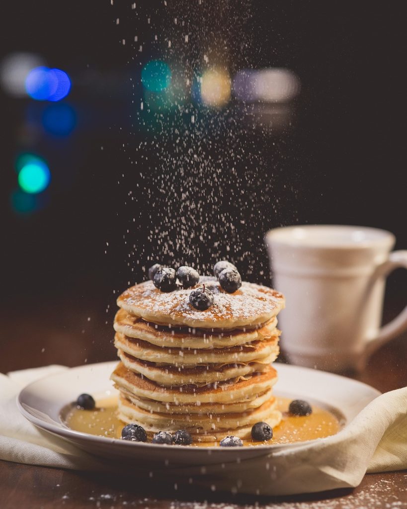 Desayuno de pancakes o tortitas con arándanos, azúcar, natillas y chocolate
