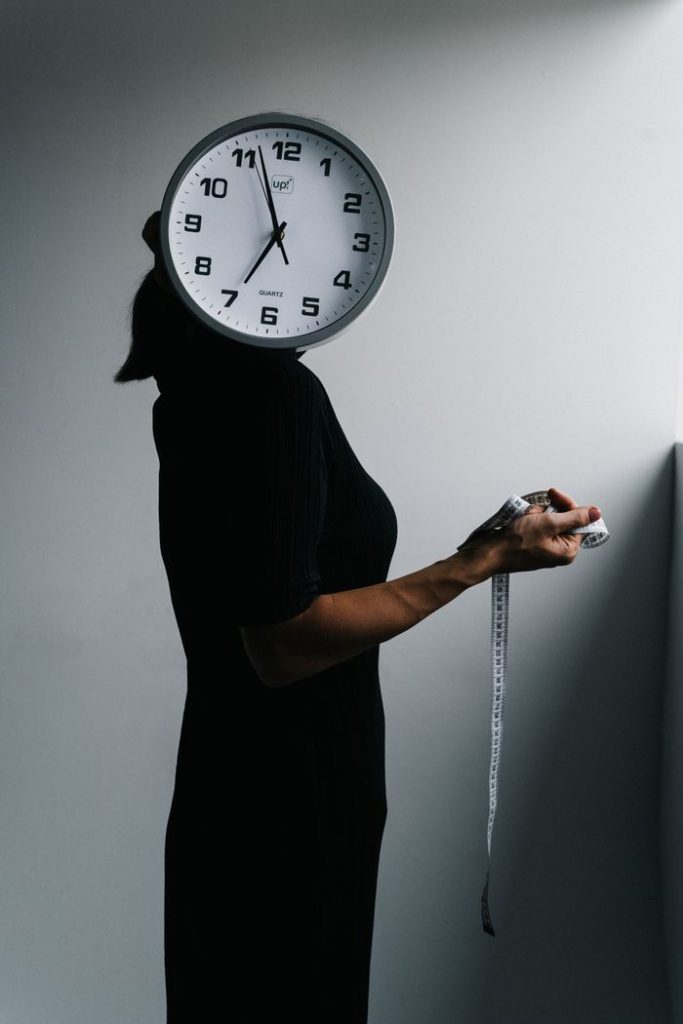 Mujer sosteniendo una cinta métrica con un reloj que le tapa la cabeza como metáfora de la influencia de los ritmos circadianos en el peso
