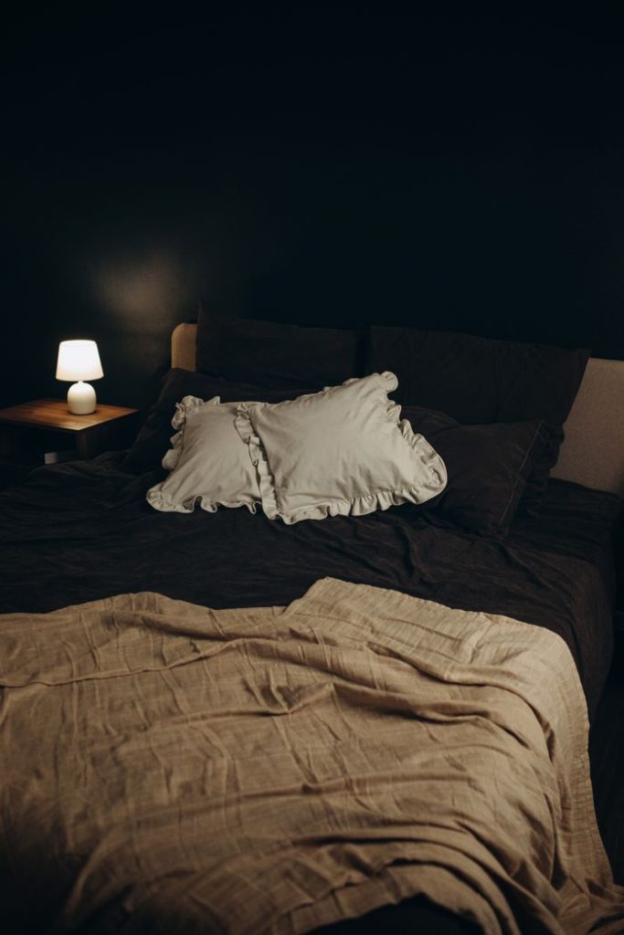 ¿Te despiertas empapada y no puedes volver a dormir? Por qué los sudores nocturnos rompen tu descanso dos veces Elegant bedroom setup featuring a soft, cozy bed with a lit bedside lamp creating a warm ambiance.
