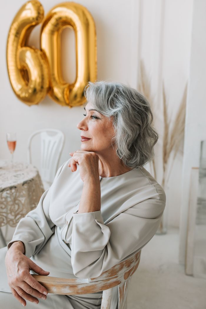 A graceful senior woman seated indoors, reflecting on her 60th birthday with champagne.
