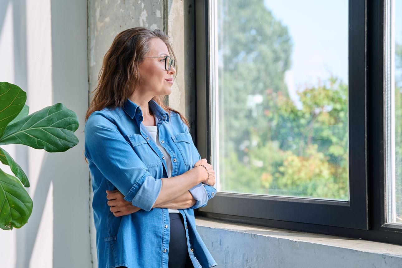 Síntomas de la perimenopausia: por qué a veces tardamos años en relacionarlos Mujer con gafas, atractiva, mirando pensativa por la ventana